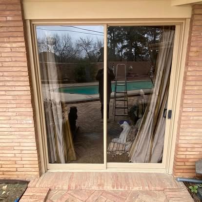 A sliding glass door with beige frames looking out onto a brick patio and a swimming pool.