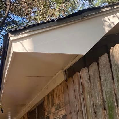Close-up of a white painted roof soffit and fascia board extending over a weathered wood fence and brick wall.