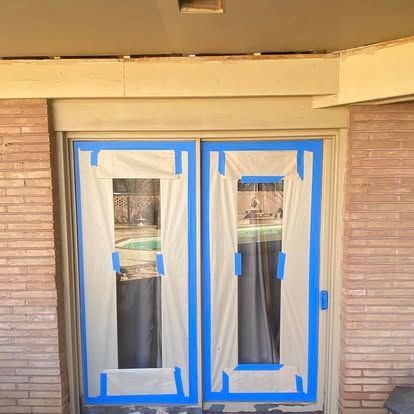 Double glass doors covered in protective plastic and blue painter's tape, ready for a painting project.