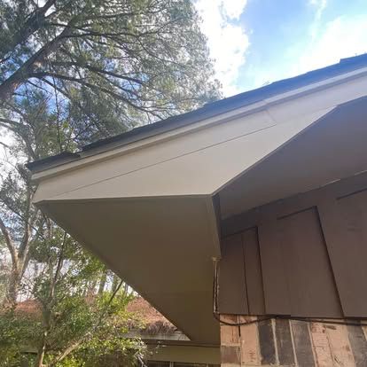 A low-angle view of a beige roof overhang and fascia board above a brown-paneled exterior wall with brick accents.