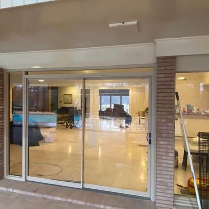 A sliding glass door opening to a bright, tiled interior room with a large window and a view of an outdoor area.