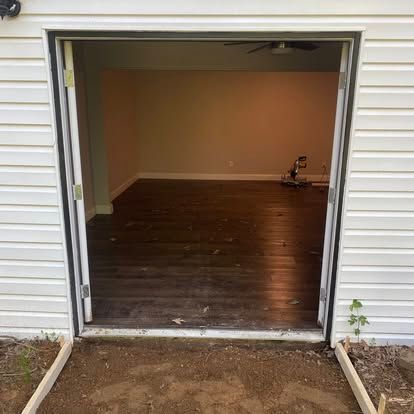 A view from outside looking into an open doorway of a house with dark wood-style floors and a ceiling fan.