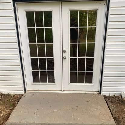 White French patio doors with glass panes set in white siding, leading out to a simple concrete doorstep.