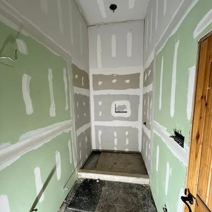 A narrow, unfinished shower stall framed with green drywall and white joint compound in a room under construction.