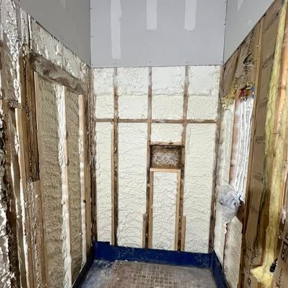 Interior wall framing with spray foam insulation between studs and a small recessed niche in a residential space.