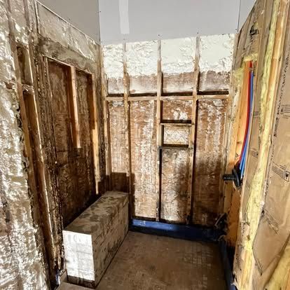 A construction site view of a wall frame with spray foam insulation, a concrete block, and exposed wiring.