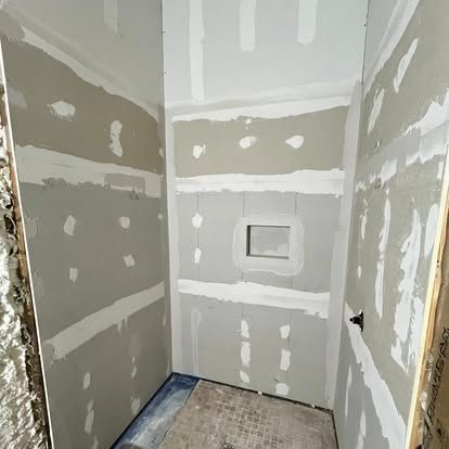 A walk-in shower area under construction with grey wallboard, taped joints, and a recessed shower niche in the back wall.