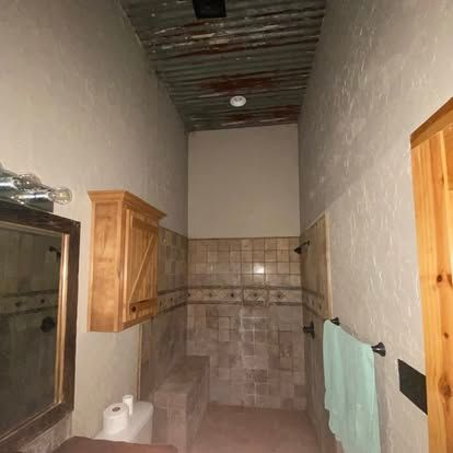 A bathroom with a wooden medicine cabinet, a tiled shower area, a rustic corrugated ceiling, and a light green towel.