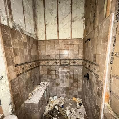 A partially demolished shower stall with brown tiled walls and a built-in bench, surrounded by exposed wall framing.