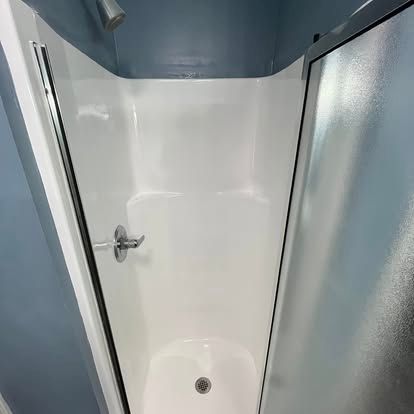 A white fiberglass shower stall with a single handle fixture and a drain, set against blue-painted walls.