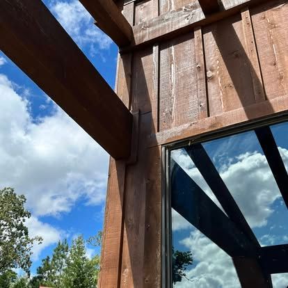 Low-angle view of a wooden structure with beams extending outward against a bright blue, cloudy sky.