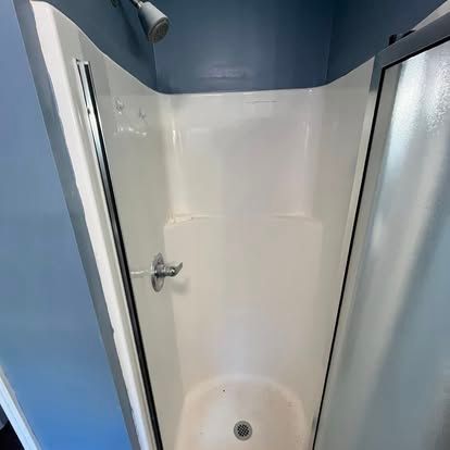 A small corner shower stall with white walls and base, a chrome faucet, and glass doors against blue bathroom walls.