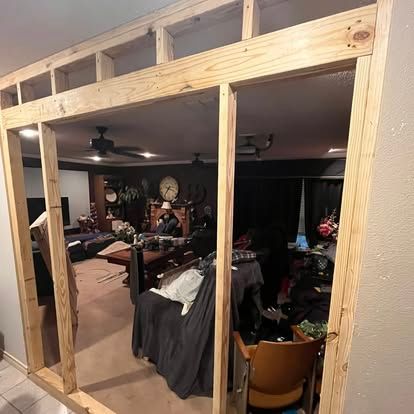 A newly constructed wooden door frame and header section installed in a wall opening, overlooking a furnished living room.