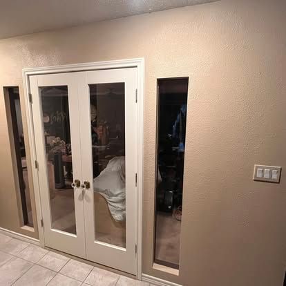 White French doors with side windows and light switches on a beige wall.