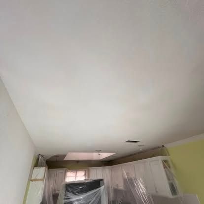 A kitchen ceiling during renovation, showing fresh white paint and plastic sheeting covering cabinets below.