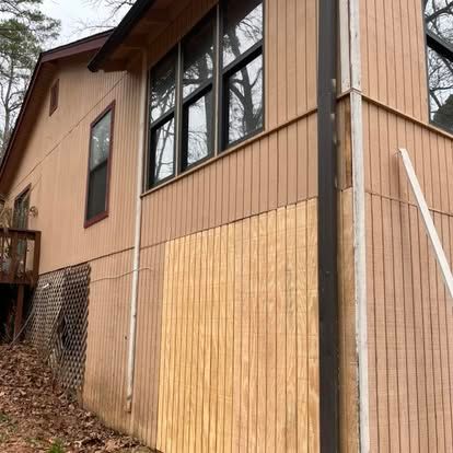 A tan house exterior with wood paneling, featuring a new, unpainted patch of wood siding on the lower wall.