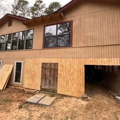 A beige house with wood siding, large windows, a wooden door, and a partially open garage area under construction.