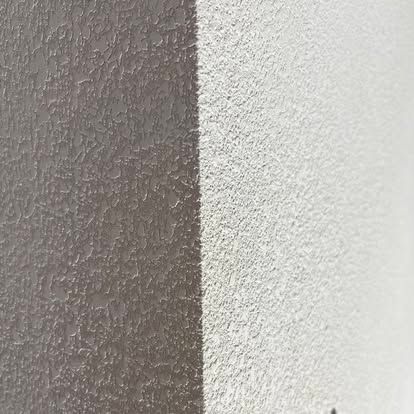 A split-view close-up of a textured wall, showing a dark gray surface on the left and a white surface on the right.