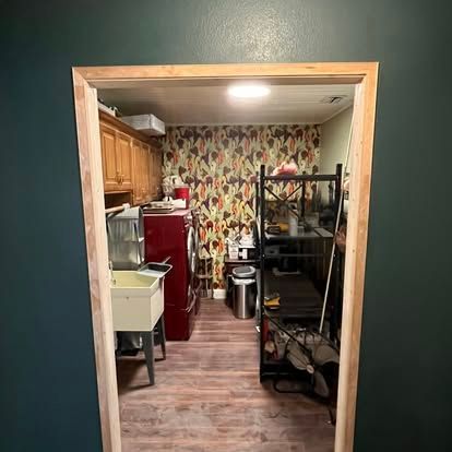 An unfinished doorway frames a laundry room featuring patterned wallpaper, a red washer, and a utility sink.
