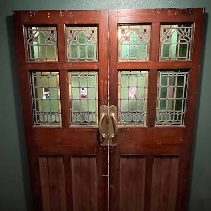 Double wooden doors with brass handles and rectangular stained glass windows in a mix of clear, green, and red glass.