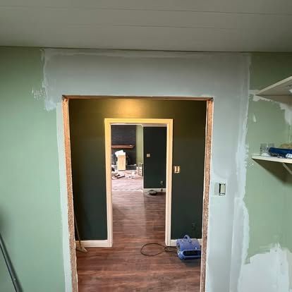 A doorway frame in a sage green wall, partially sanded and prepped for painting around the molding.