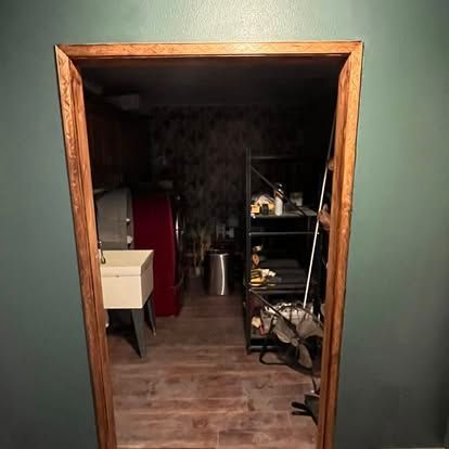 A doorway with wooden trim opens into a utility room containing a utility sink, a red appliance, and metal shelving.