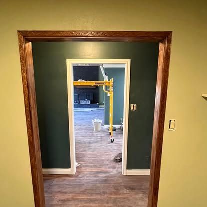 A doorway with dark wood trim reveals a room with dark green walls, wood-look flooring, and yellow scaffolding inside.