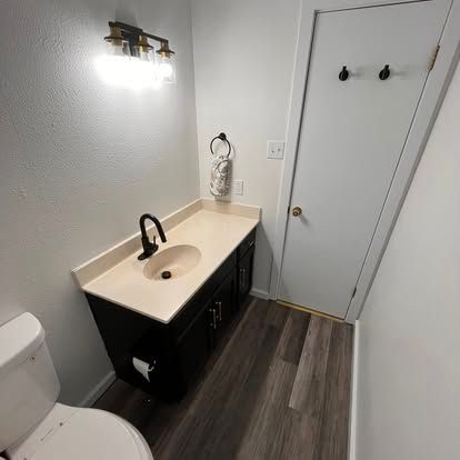 A modern small bathroom featuring a white vanity with a black cabinet, a neutral countertop, and wood-look flooring.