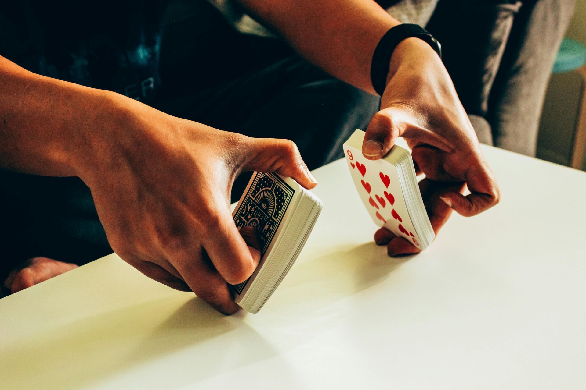 Hands holding two halves of a deck of playing cards on a white table, ready to perform a magic trick.