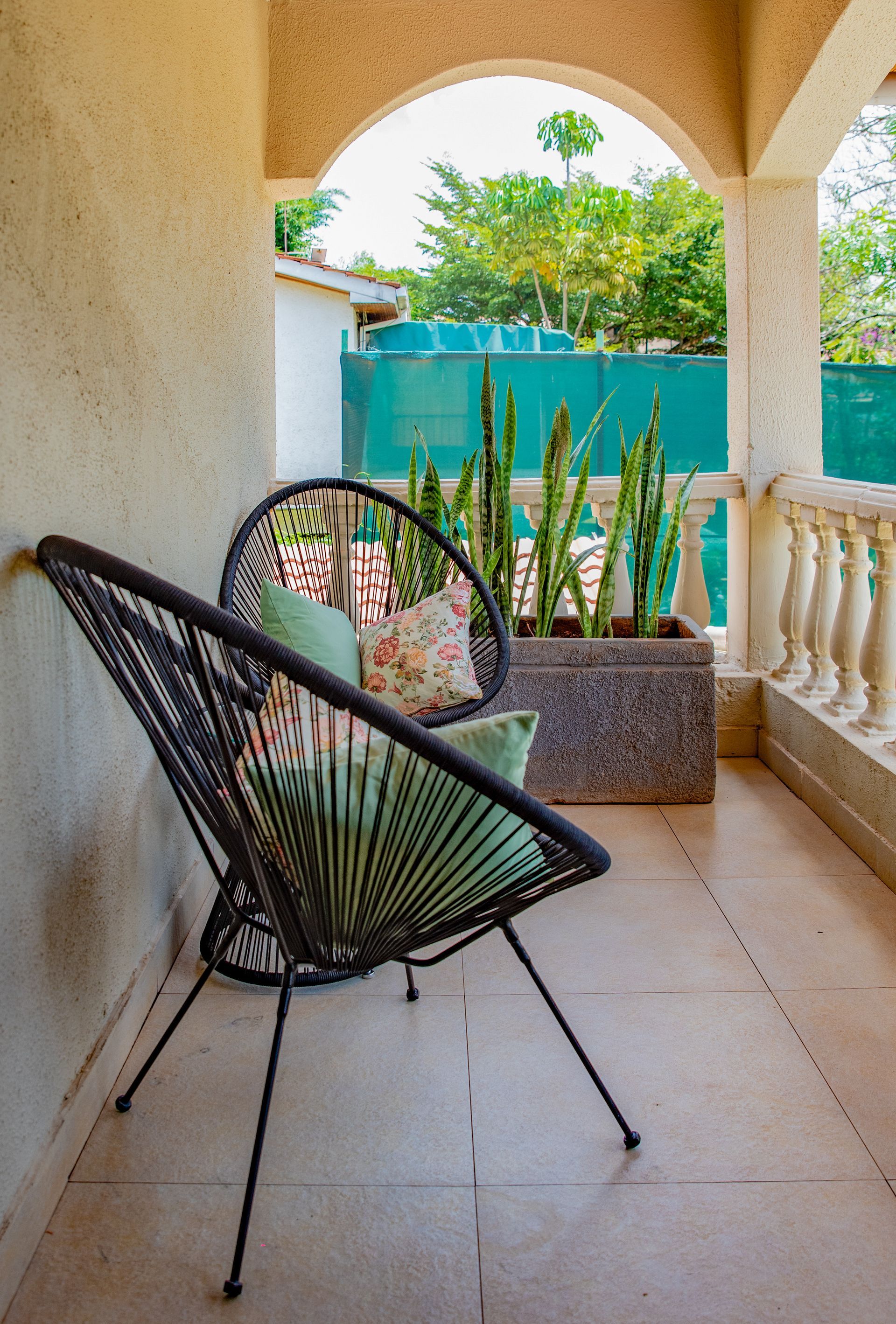 Two black woven chairs on a porch, facing a garden with tall green plants.