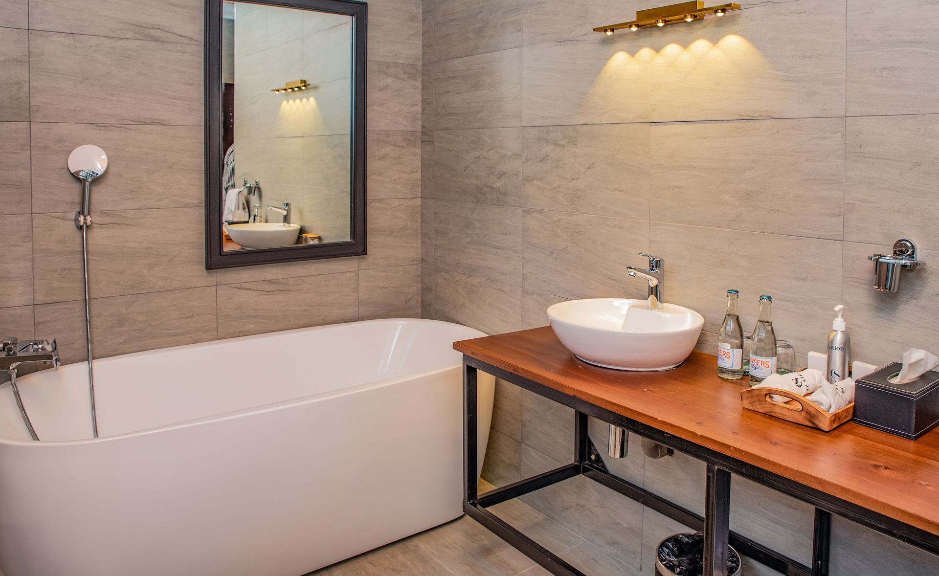 Bathroom with a bathtub, a sink on a wooden counter, and a wall-mounted showerhead. walls and a large mirror are visible.