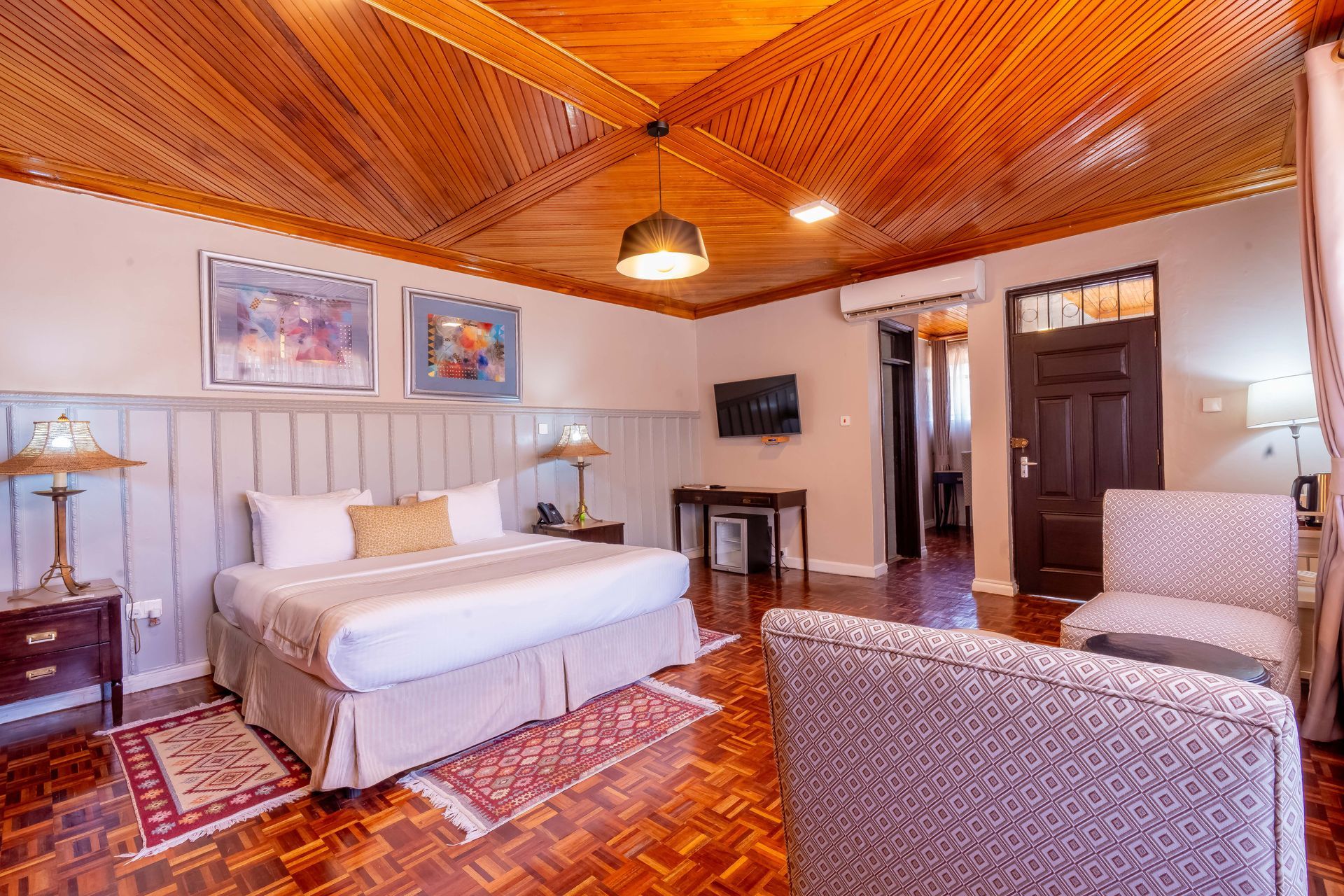 Hotel room with a large bed, wooden ceiling and floor, and patterned furniture.