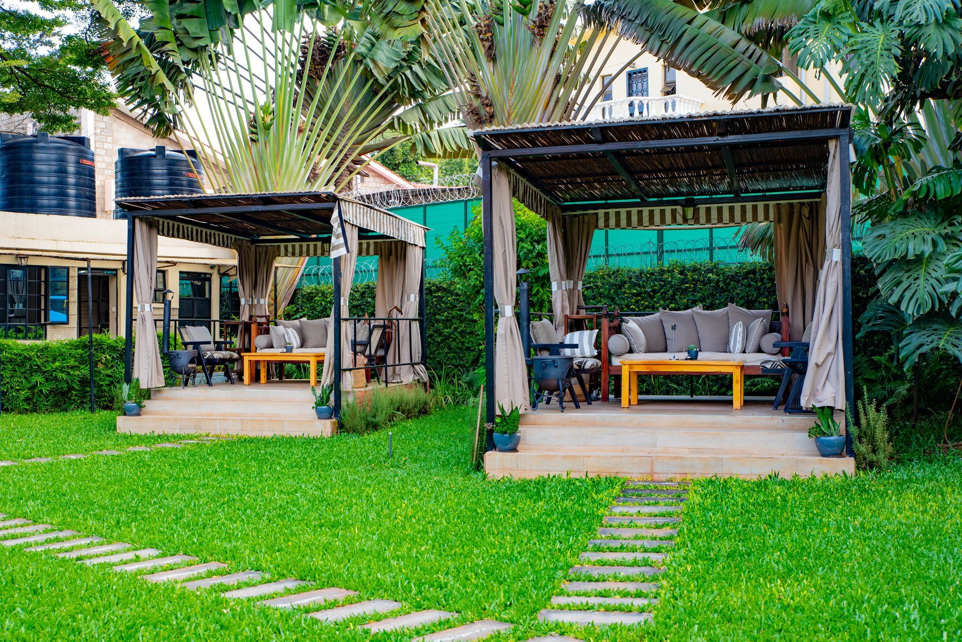 Two outdoor lounge areas with couches and tables under shaded canopies on a grassy lawn.