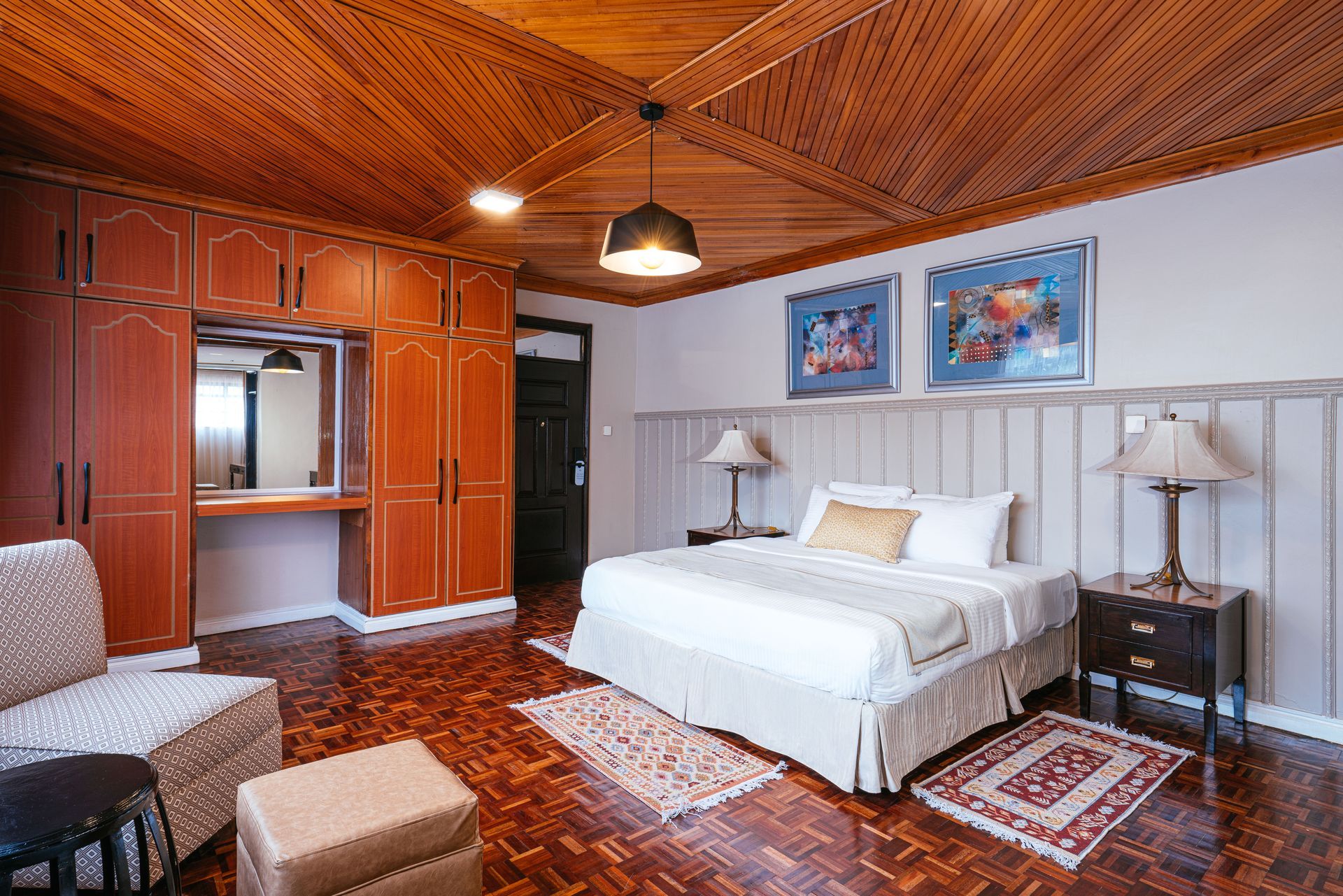 Bedroom with wooden details: ornate ceiling, wardrobe, bed with lamps, and patterned rugs.