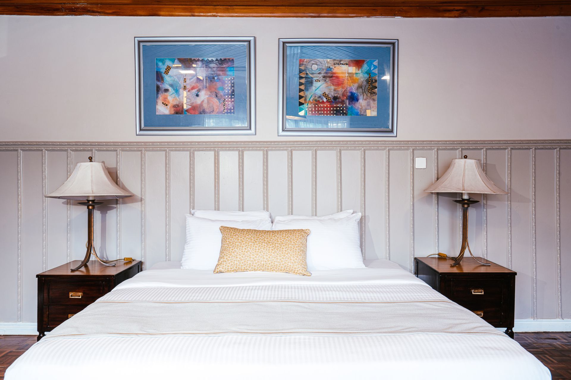 A bedroom with a bed, two nightstands with lamps, and two framed art pieces. The headboard has vertical panels.