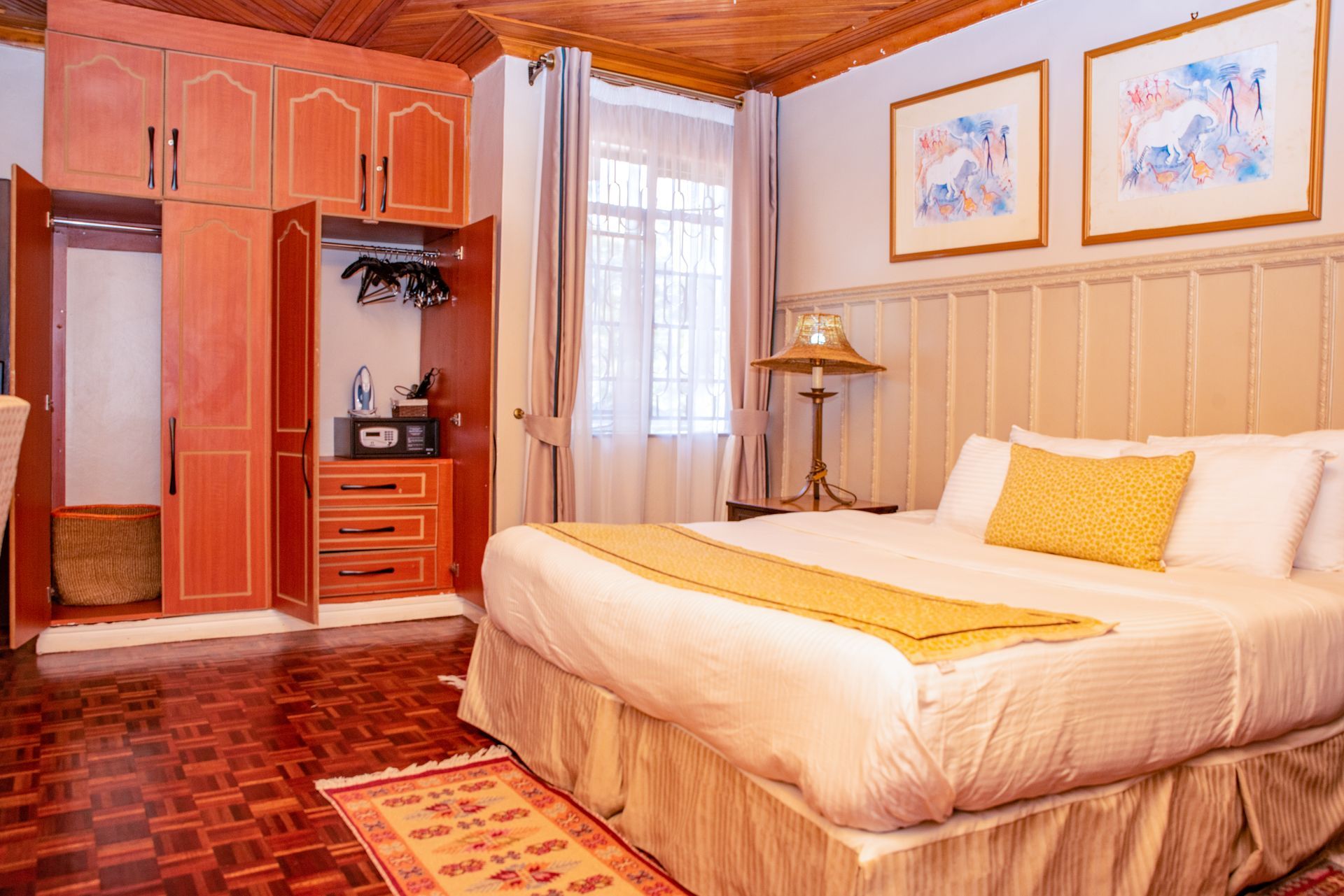 Hotel bedroom with a large bed, wooden wardrobe, and artwork on the wall. The room has warm lighting and wood flooring.