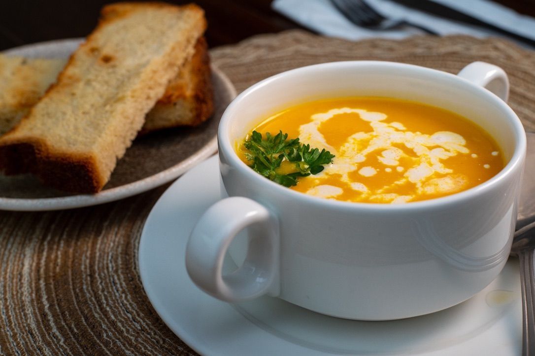 A bowl of orange soup with cream swirl, parsley garnish, and toast slices.