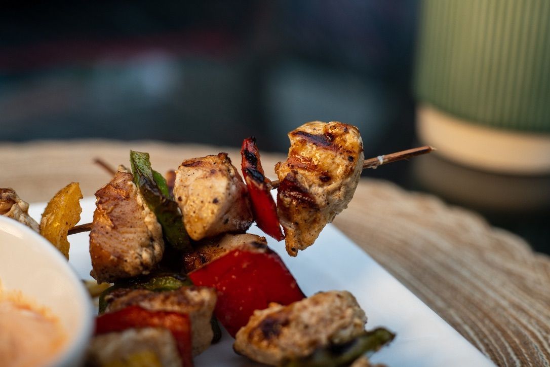 Chicken and vegetable skewers on a white plate with a dipping sauce. Grilled chicken and colorful peppers.