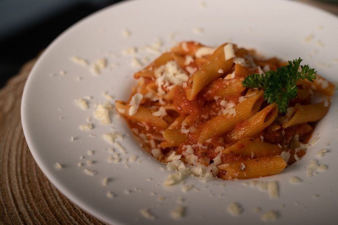 Penne pasta in tomato sauce, sprinkled with cheese and garnished with parsley, served on a white plate.