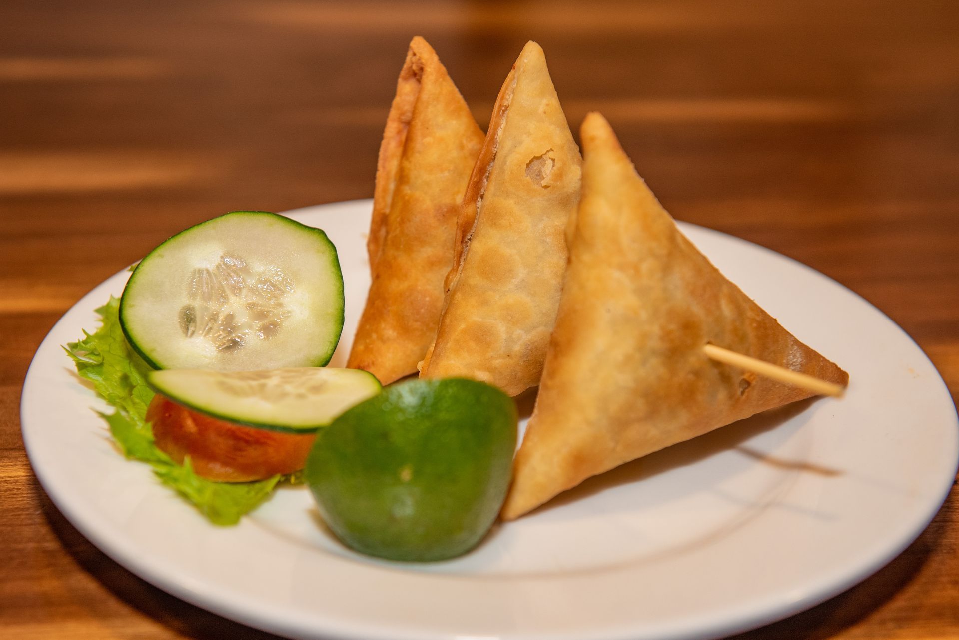 Plate of golden samosas with lime, cucumber, and tomato slices on a white plate.