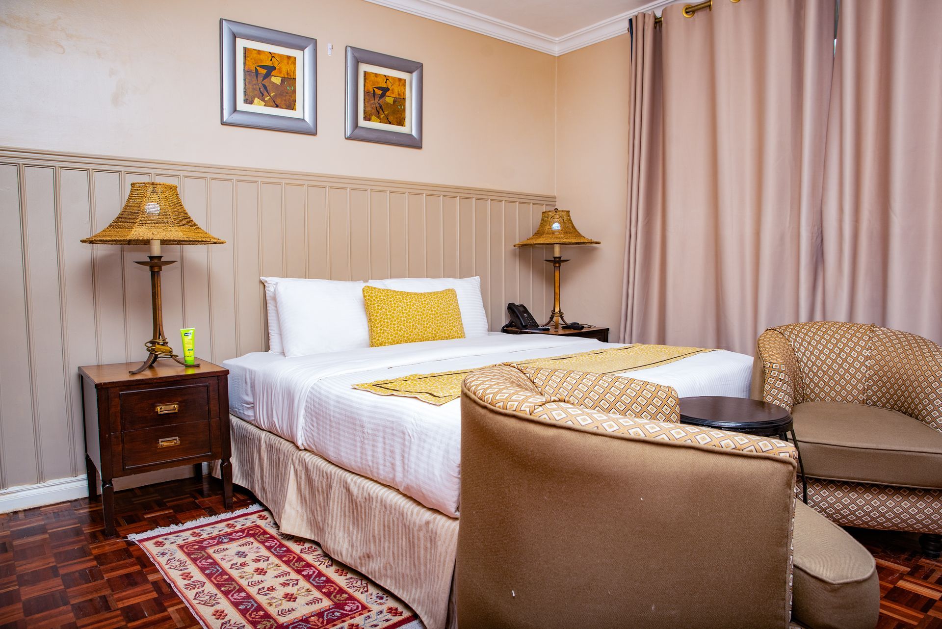 Hotel room with a bed, two lamps, two chairs, and a small rug.