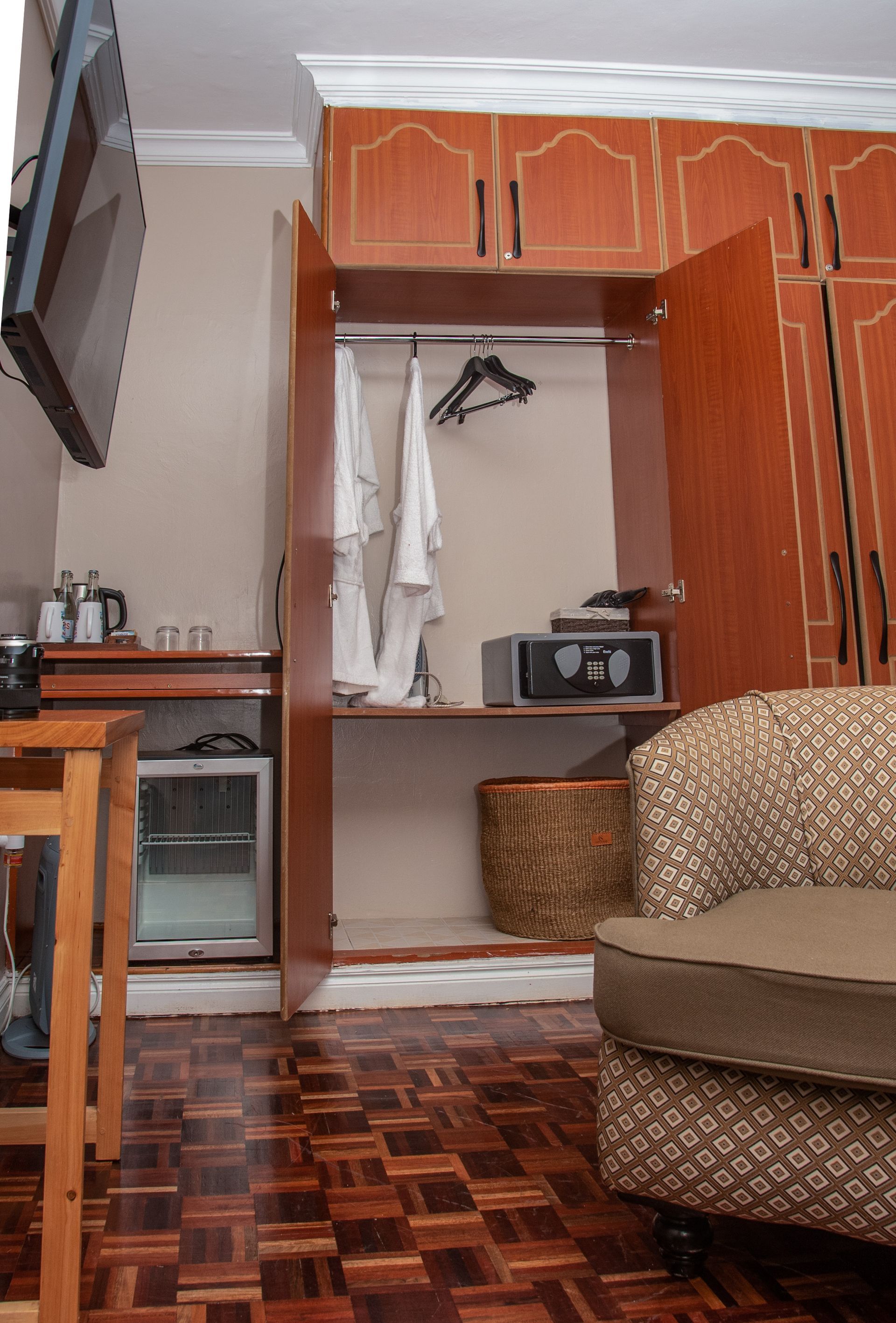 Hotel room with wardrobe and safe. Includes a small fridge, arm chair, and wooden flooring.