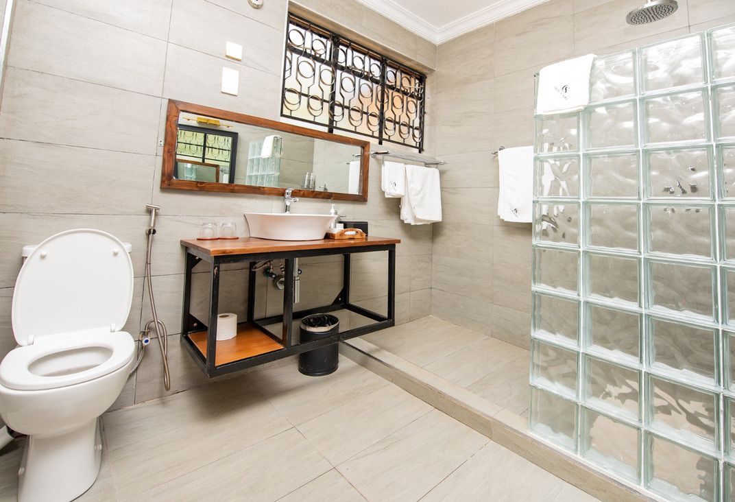 Bathroom with a toilet, floating vanity with a sink, and a shower with a glass block wall. The walls and floor are tiled.