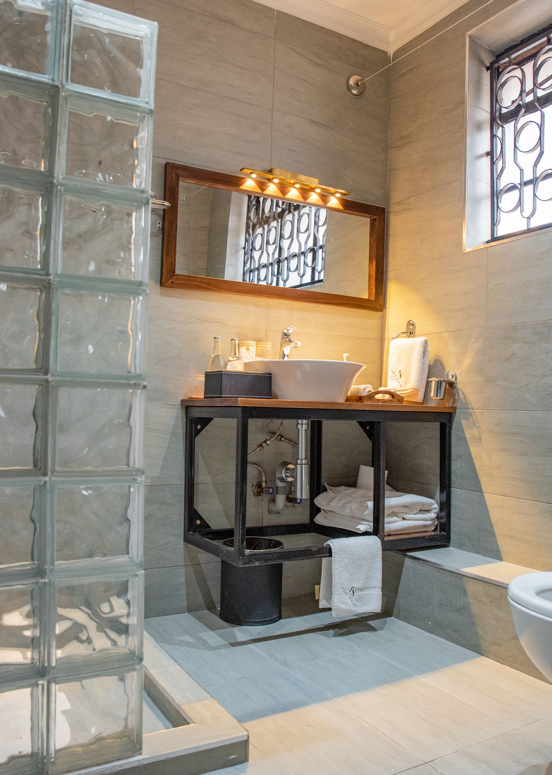 Bathroom with a block shower, industrial-style sink, and a window with metal bars. The walls and floor are light-colored.