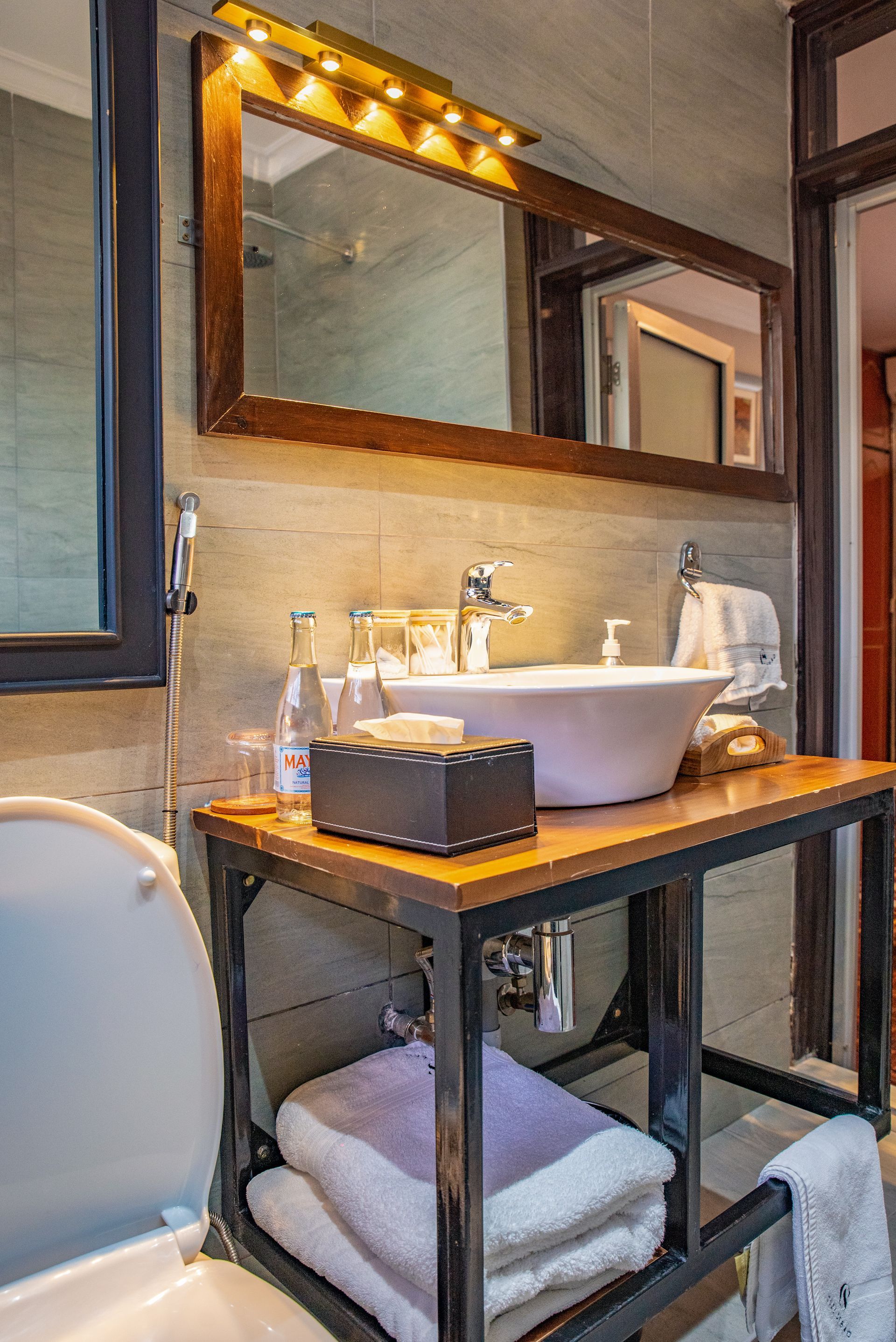 Bathroom with a white sink, wooden vanity, and a large mirror with lights above it. A toilet is in the foreground.