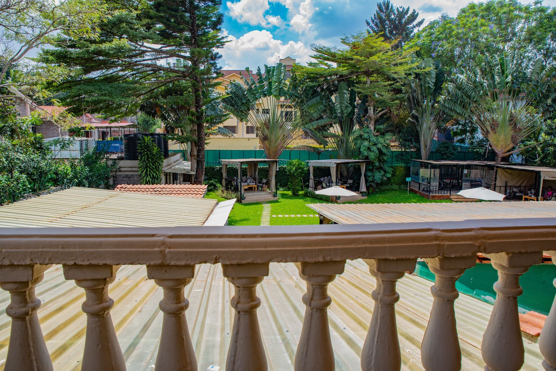 Balcony view overlooking a lush backyard with trees, gazebos, and green grass under a partly cloudy sky.