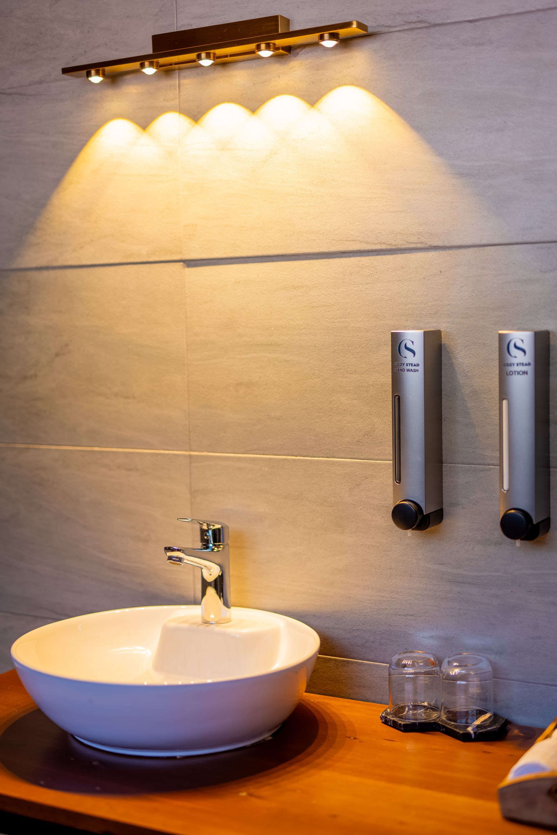 Bathroom sink with a white bowl, chrome faucet, and soap dispenser, lit by a warm light fixture.
