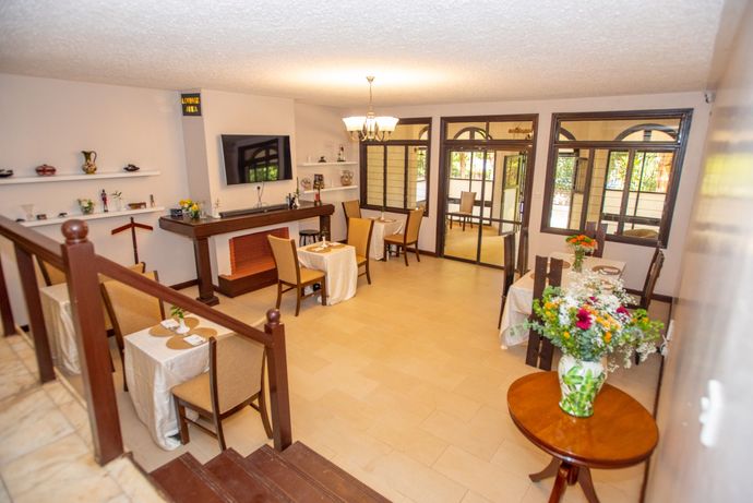 Cozy Stead spacious living room with wooden railings, chairs, flowers, and large windows overlooking greenery