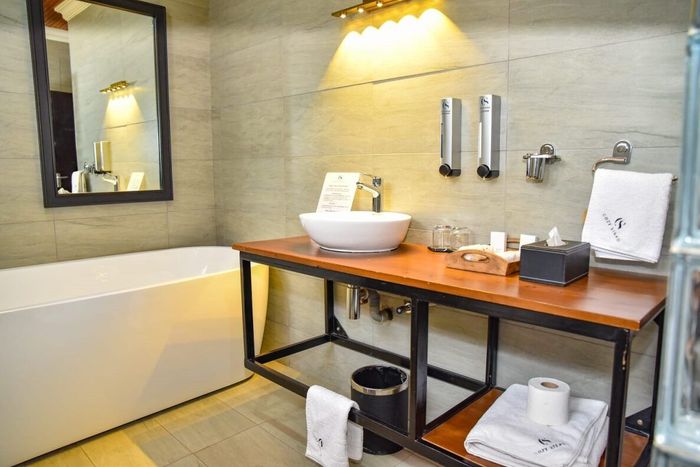 Cozy Stead Modern bathroom with bathtub, wooden vanity, vessel sink, mirror, and warm wall lighting.