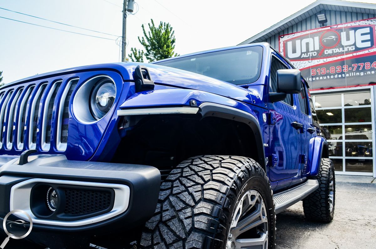 Blue lifted Jeep Wrangler parked outside a dealership, front view with oversized off-road tires